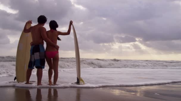 Пара с доской для серфинга на пляже — стоковое видео