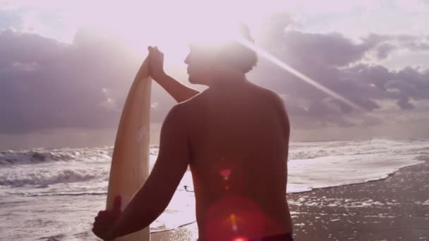 Мужчина держит доску для серфинга на пляже — стоковое видео