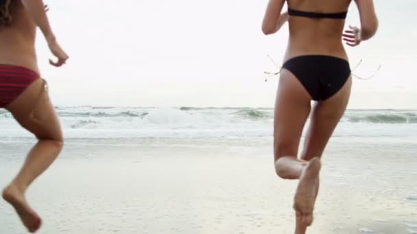 Молодые девушки в бикини держатся за руки и бегут в океан — стоковое видео
