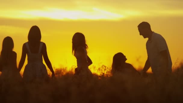 Părinți cu fiice pe pajiște la apusul soarelui — Videoclip de stoc