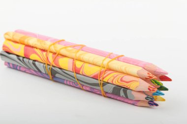 Fıçılarda parlak mermer desenli renkli ahşap kalemler, beyaz arka planda turuncu bir lastik bantla bağlanmış..