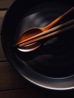 Tahta kaşık, yemek çubuğu ve porselen tabak.