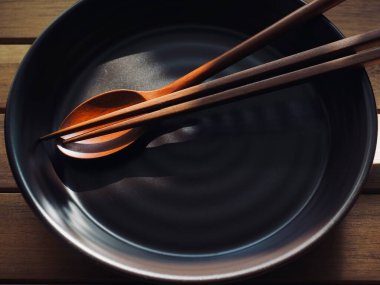 Tahta kaşık, yemek çubuğu ve porselen tabak.