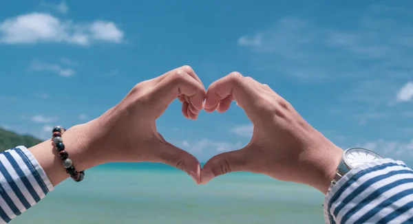 Woman hand do heart shape on blue sky and beach background.