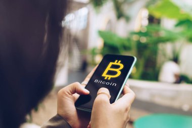 Kadın akıllı telefon kullanarak internet üzerinden para kazanıyor. Tabela simgesi olan bitcoin alıyor. Akıllı telefon kavramında iş fintech teknolojisi.