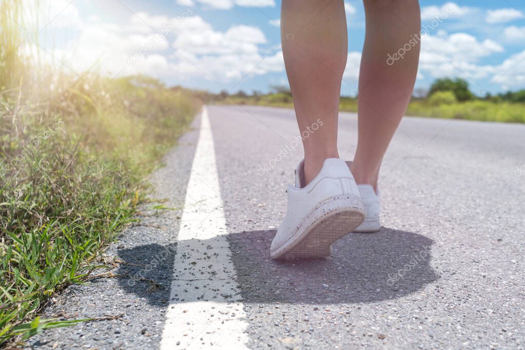 Woman is walking on small country road street with blue sky background.
