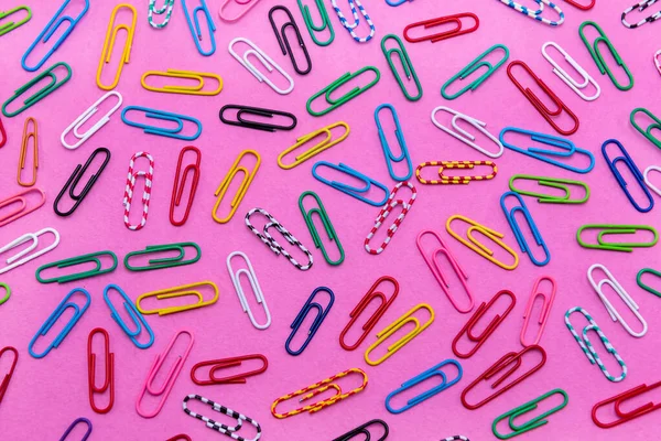 Colored paper clips are scattered on the background of pink flowers