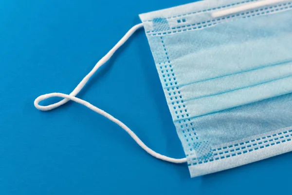 A protective face mask lies on a blue background close up