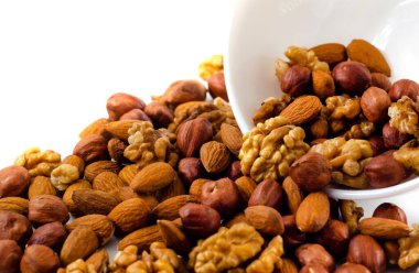 Fındık, badem ve ceviz beyaz arka planda tabağın etrafına saçılmış. Cevizler lezzetli, sağlıklı ve besleyicidir.