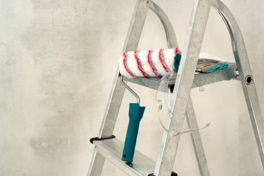 Merdiven, boya silindiri, beton bir duvarın arka planında fırça. İnşaat ve boyama işleri