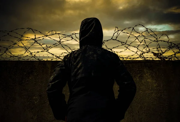 犯罪者だ 刑務所だ 日没時に有刺鉄線のある刑務所の壁の男 犯罪と無法 — ストック写真