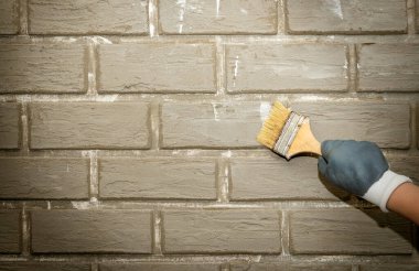 Onarım. Elli tuğla duvar ve tuğlaları boyayan boya fırçası. Boyama işi.