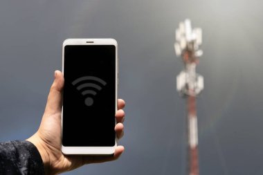 Bir el, kablosuz iletişim istasyonunun arka planında bir cep telefonu tutuyor. Yüksek hızlı veri transferi. Teknolojiler