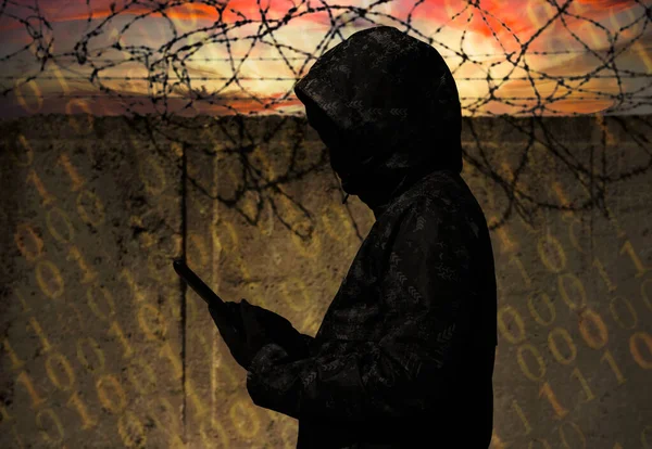 Bir hacker dikenli telle bir hapishanenin duvarına karşı duruyor. Siber güvenlik. Cezaevi