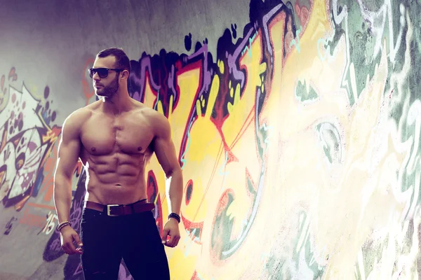 Young fit macho man posing in front of graffiti wall — Stock Photo, Image