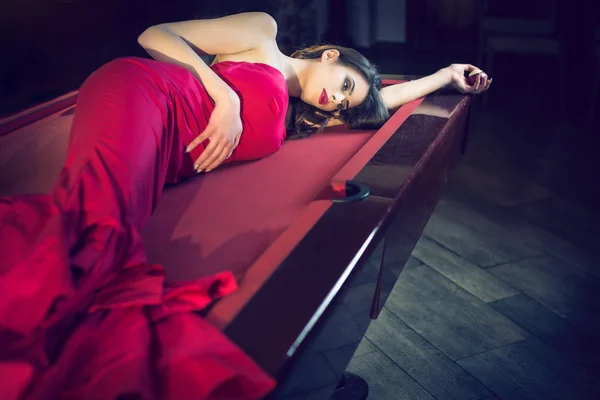 Menina vestido vermelho deitado na mesa de bilhar — Fotografia de Stock