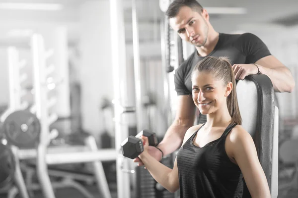 Žena, která dělá bicep kudrlinky v tělocvičně s její osobní trenér — Stock fotografie