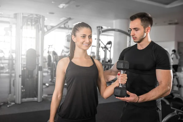 Mulher fazendo cachos de bíceps no ginásio com seu personal trainer — Fotografia de Stock