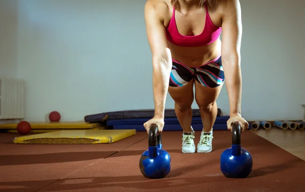 Fitness žena, která dělá push ups s kettlebells — Stock fotografie