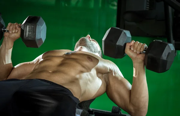 Hombre haciendo mancuerna prensa mientras se acuesta —  Fotos de Stock