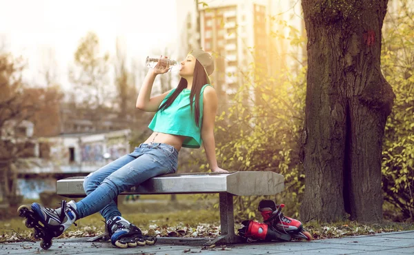 Roller girl drinking water on bench — Stock Photo, Image