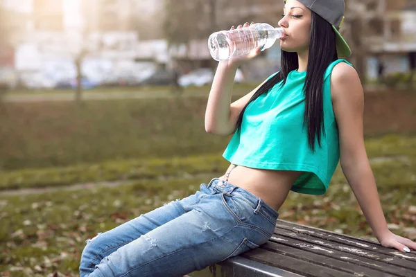 Roller dívka pitné vody na lavičce — Stock fotografie