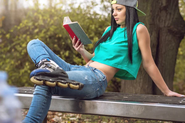 Девушка в джинсах читает книгу о скамейке — стоковое фото