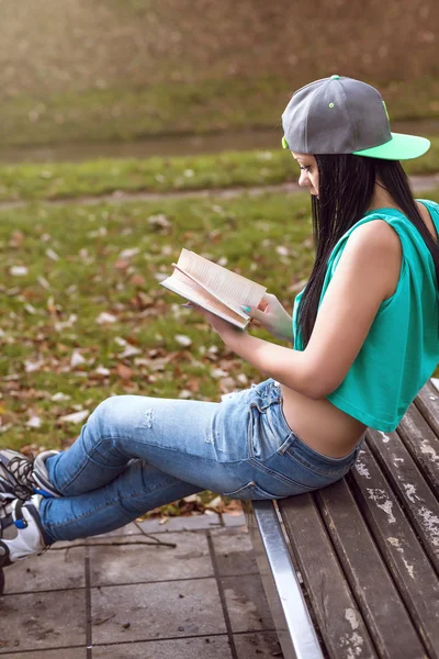 Dziewczyna w dżinsy, czytając książkę na ławce — Zdjęcie stockowe