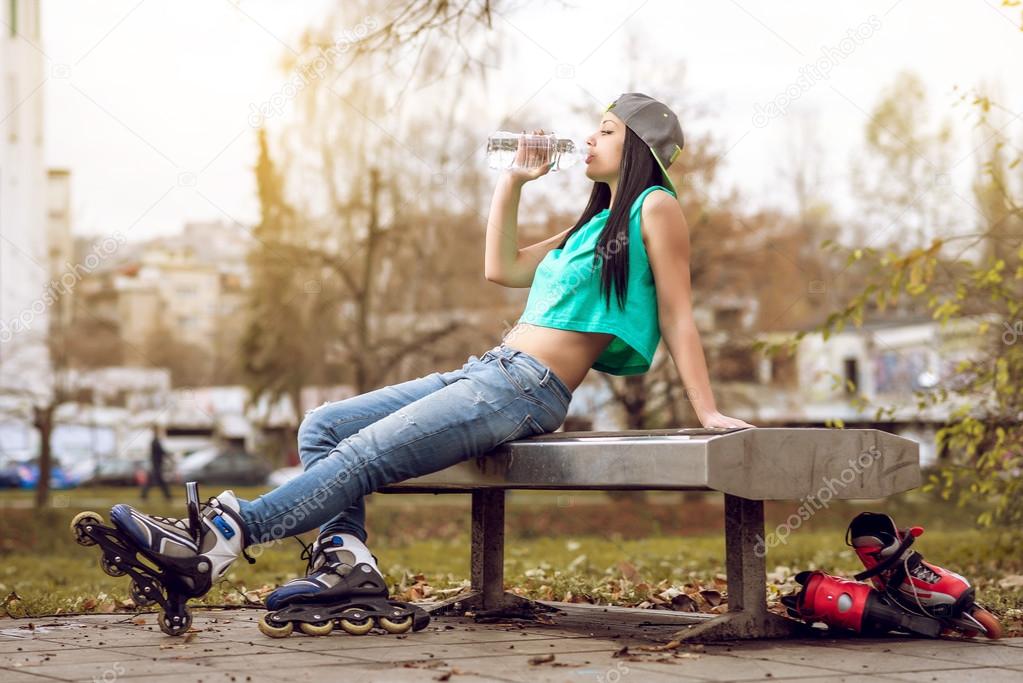 Roller girl drinking water on bench