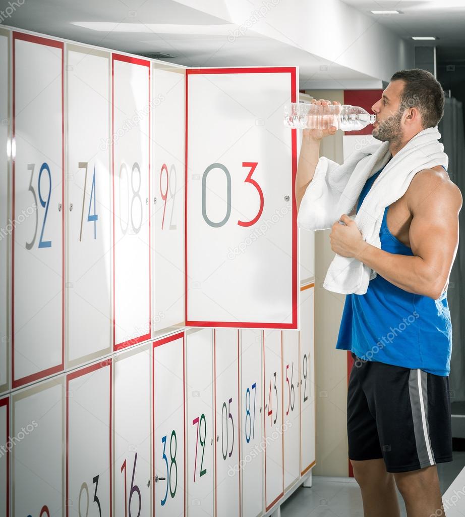 Young adult man drinking water in locker room