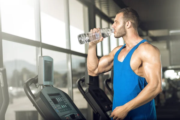 Hombre joven bebiendo agua en el gimnasio — Foto de Stock