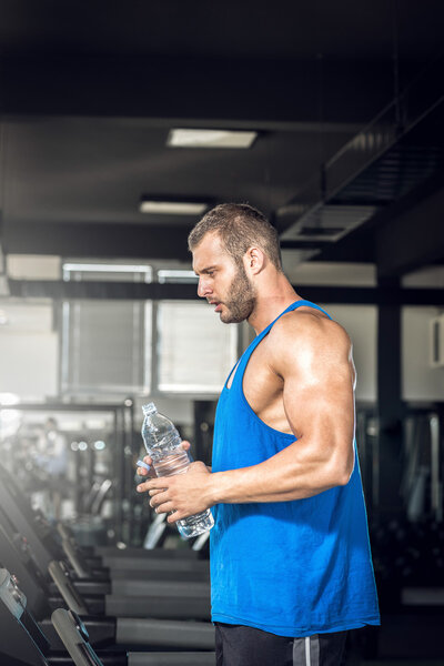 Young man drinking water in gym