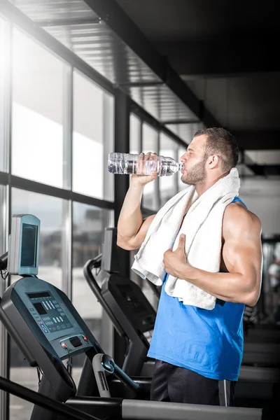 Hombre joven bebiendo agua en el gimnasio — Foto de Stock