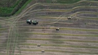 Traktör ve çim biçme makinesi yuvarlak balyalara saman toplayıp paketliyor. Kesilen çimlerin tarlalardan toplanması, sıkıştırılması ve taşınması