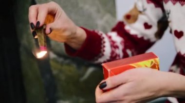Bir kadın uzun süre yanan bir kibrit yakar ve şöminede bir ateş yakar.