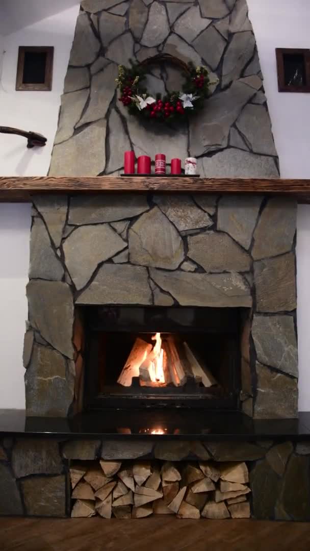 Fire burn in a fireplace decorated with wreath and candles on Christmas eve. New Year holidays celebration. Vertical video — Stock Video