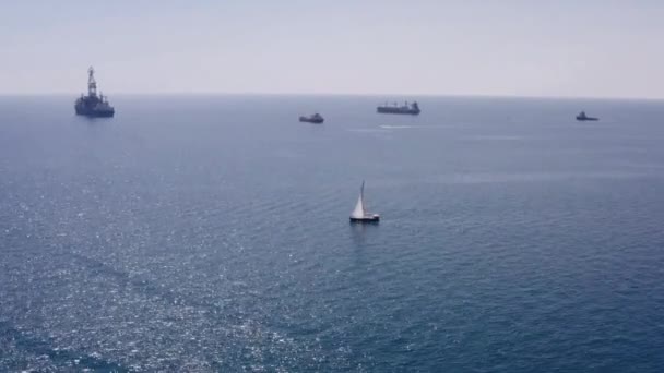 晴れた日に海上港を出発する大型貨物船の空中ビューと小さなボートは湾に帆。輸送物流の概念 — ストック動画
