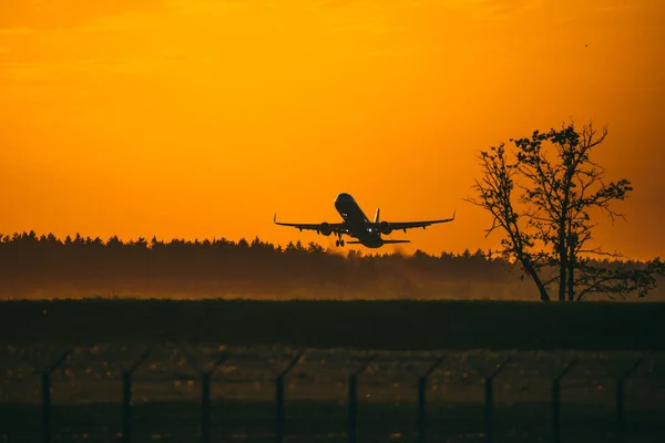 O avião descola no aeroporto ao pôr-do-sol e laranja ensolarado. — Fotografia de Stock
