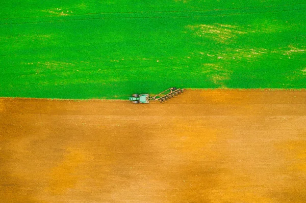 Aerial photo of brown and green field. Tractor harrows the ground. Horizontal pattern. — Stock Photo, Image