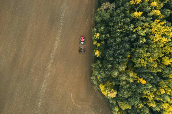 Фермер в тракторі готує сільськогосподарські угіддя з посівом на наступний рік. Барвистий осінній ліс . — стокове фото