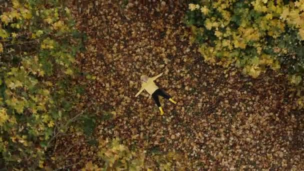 Lockiges Mädchen liegt auf dem hellen Herbstlaub im Park und träumt, von einer Drohne aus geschossen. Herbstkonzept — Stockvideo