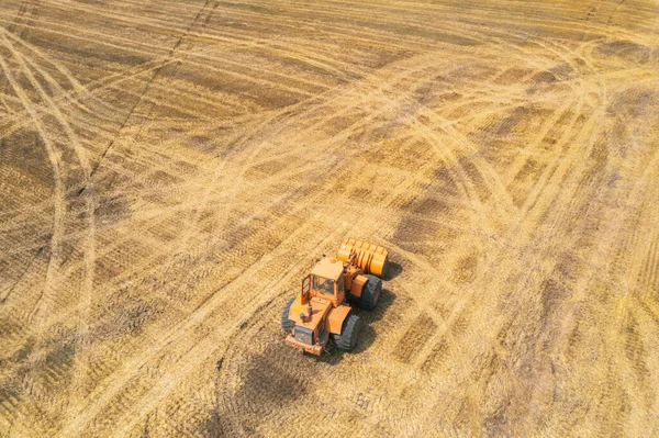 Orangener Traktor fährt durch das gemähte Weizenfeld. Bauern bei der Arbeit. Erntezeit in der Landwirtschaft. — Stockfoto