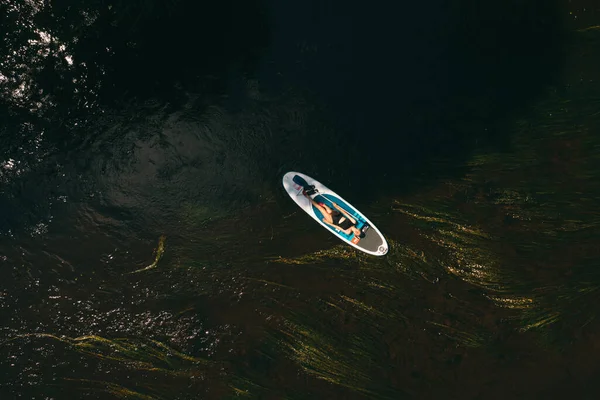 Bovenaanzicht van een meisje dat in rivierwater zwemt op een surfplank — Stockfoto
