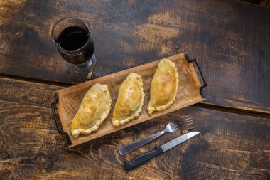 Traditional baked Argentine and Uruguay empanadas savoury pastries with meat beef stuffing against wooden background. clipart