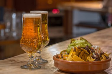 Nachos, chilli con carne ve arka planda guacamole ile tabak.