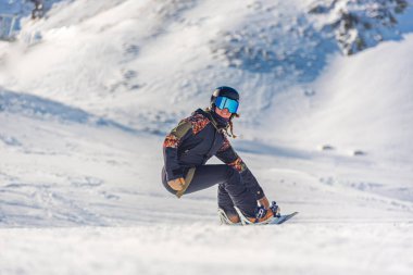 Genç kadın snowboardcu dağlarda snowboard yapıyor..