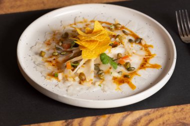 Kırmızı biberli Cod Carpaccio tabağı, kabak çekirdeği ve patates kızartması.