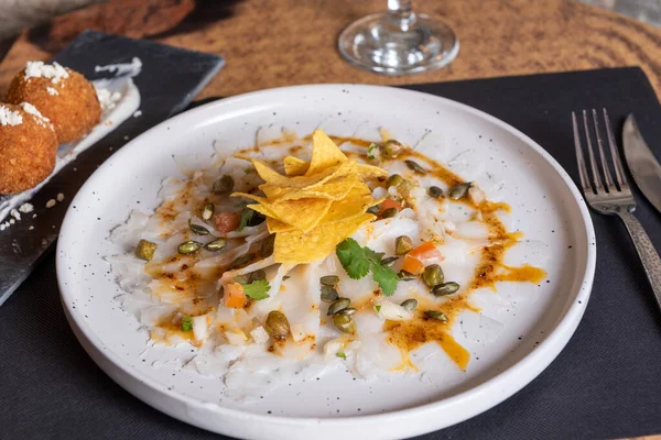 Kırmızı biberli Cod Carpaccio tabağı, kabak çekirdeği ve patates kızartması.