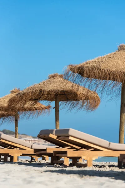 İspanya 'nın Formentera adasında güverte sandalyeleri ve saman şemsiyeleri..