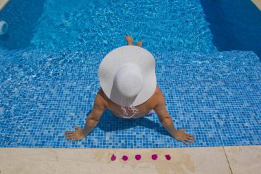 Havuzda dinlenen beyaz şapkalı genç bir kadın.